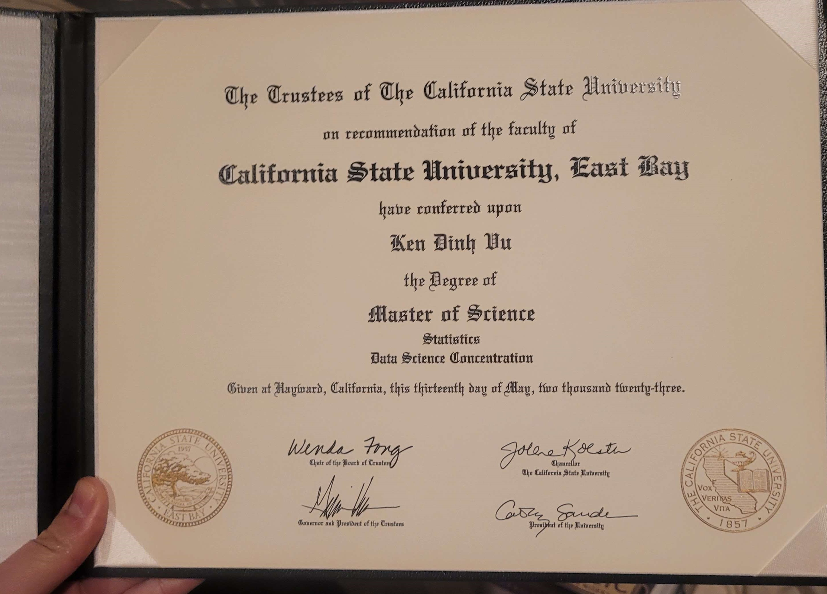 A picture of a master's degree diploma from California State University - East Bay that reads, 'The trustees of the California State University on recommendation of the faculty of California State University - East Bay have conferred upon Ken Dinh Vu the Degree of Master of Science - Statistics, Data Science Concentration.  Given at Hayward, California, this thirteenth day of May, two thousand twenty five with signatures from the Chair of the Board of Trustees, the Chancellor of the California State University system, California State Governor and the President of the Trustees, and the President of California State University - East Bay'  To the bottom left of the diploma is the seal of california State University featuring a tree on a hill against a rising sun.  To the bottom right of the diploma is the seal of the california State University system featuring a silhuette of the state of California with the motto 'Vox Veritas Vita' and the founding year '1857' stamped at the bottom of the seal.