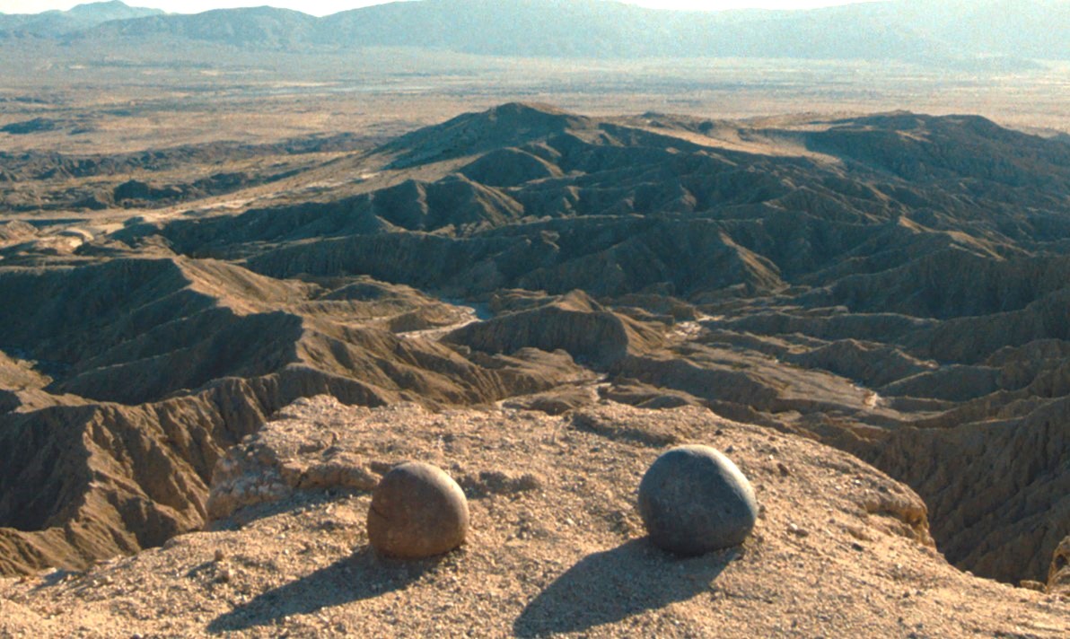 A pair of rocks at the edge of a barren sandy cliff overlooking a large gourge on a sunny day as seen in the movie 'Everything Everywhere All at Once'.