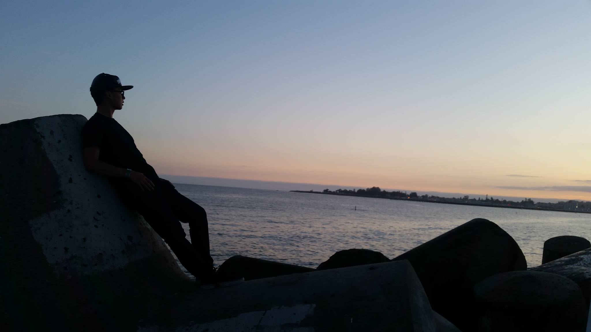A silhouette of me leaning against rocks as I look out at the ocean during a dim sunset.